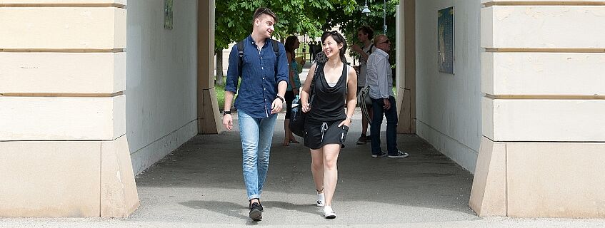 two students walk through an archway while smiling at each other